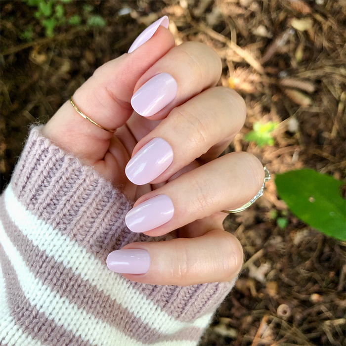 Hand with short round nails in cool lavender neutral shade wearing Sculpture Wing | Short | Round - Tab Press-On outdoors