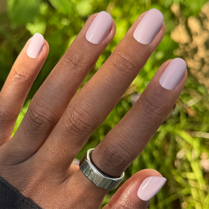 Hand wearing Sculpture Wing | Short | Round - Tab Press-On nails in cool lavender neutral shade outdoors with silver ring