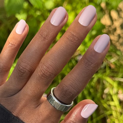 Hand wearing Sculpture Wing | Short | Round - Tab Press-On nails in cool lavender neutral shade outdoors with silver ring