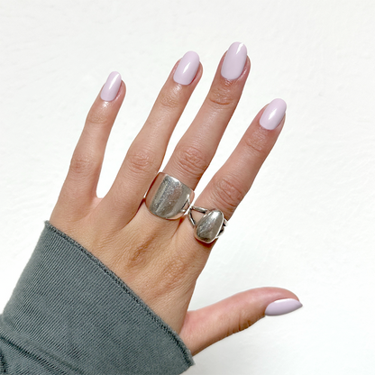 Hand with Sculpture Wing | Short | Round - Tab Press-On nails in cool lavender grey wearing silver rings and gray sleeve
