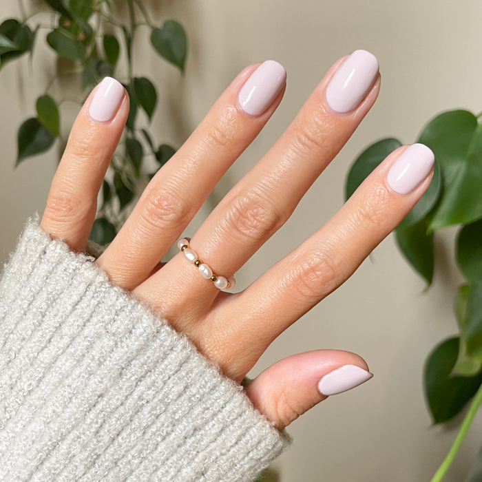 Hand wearing Sculpture Wing | Short | Round - Tab Press-On nails in soft cool lavender shade with pearl ring and cozy sweater sleeve