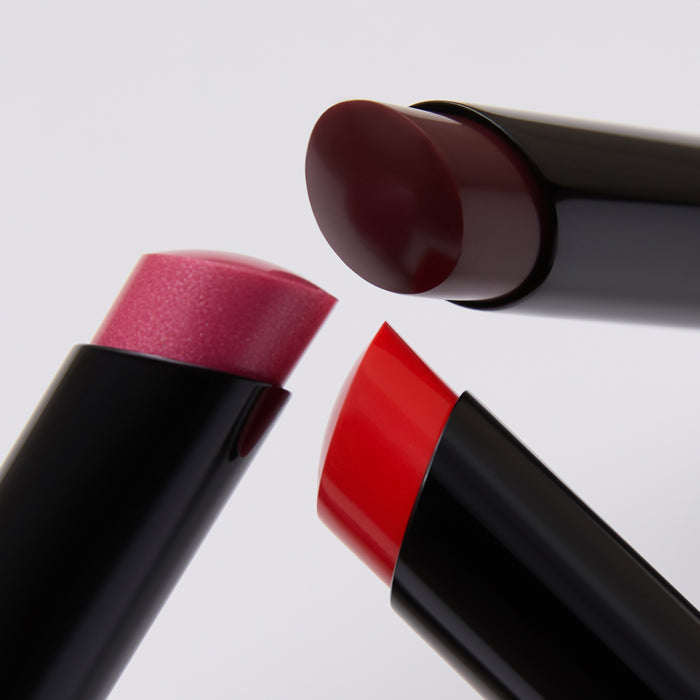 Three lipsticks in red, pink, and brown on a light gray background