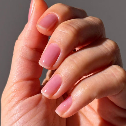 A close-up of a hand with short, manicured nails coated in LONDONTOWN Sheer Strength Nail Blush - Concord, a glossy light pink 2-in-1 nail hardener for extra strength and shine.