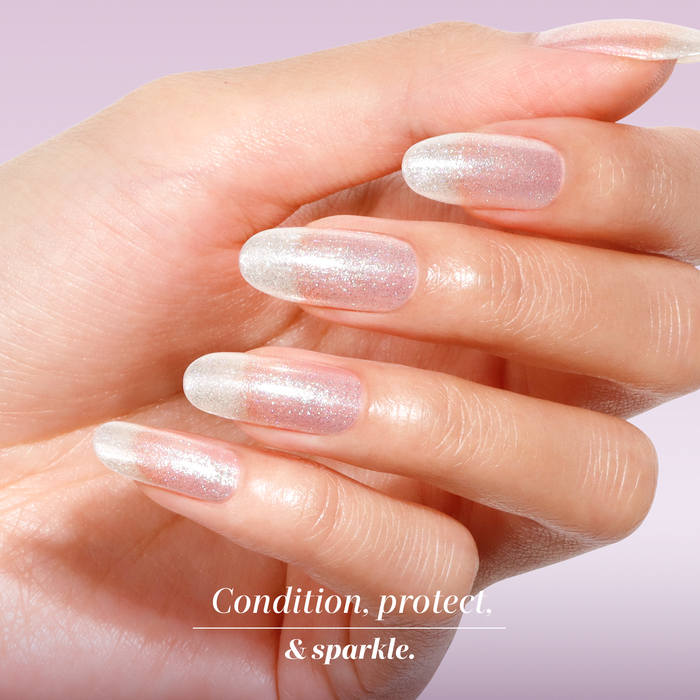 A hand with long, natural nails painted in LONDONTOWN Shimmering Nail Highlighter - Mirror Ball against a soft pink background. Text reads: "Condition, protect, & sparkle.