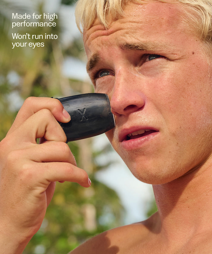 Young man applying Sun Bum Signature SPF 30 Mineral Face Stick near his eye outdoors in sunlight.