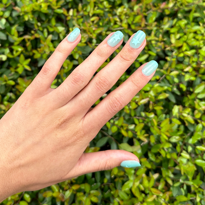 Spring Stars | Short | Squoval - Tab Press-On nails in mint pastel with embossed star accents on hand outdoors by green leaves