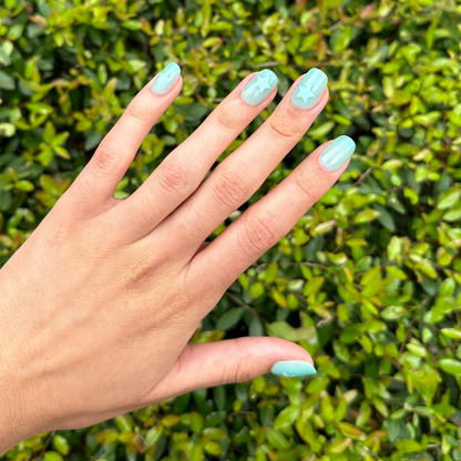 Spring Stars | Short | Squoval - Tab Press-On nails in mint pastel with embossed star accents on hand outdoors by green leaves