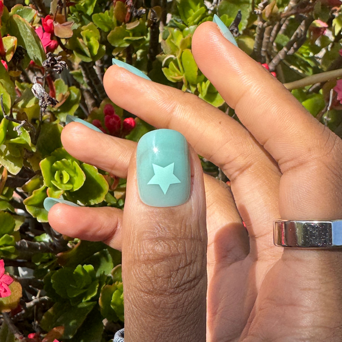 Spring Stars | Short | Squoval - Tab Press-On nails in mint pastel with turquoise star accent on thumb outdoors by green plants