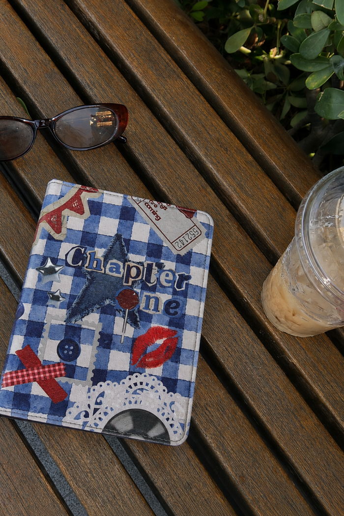 Small notebook with decorative cover on a wooden surface with glasses and a drink.