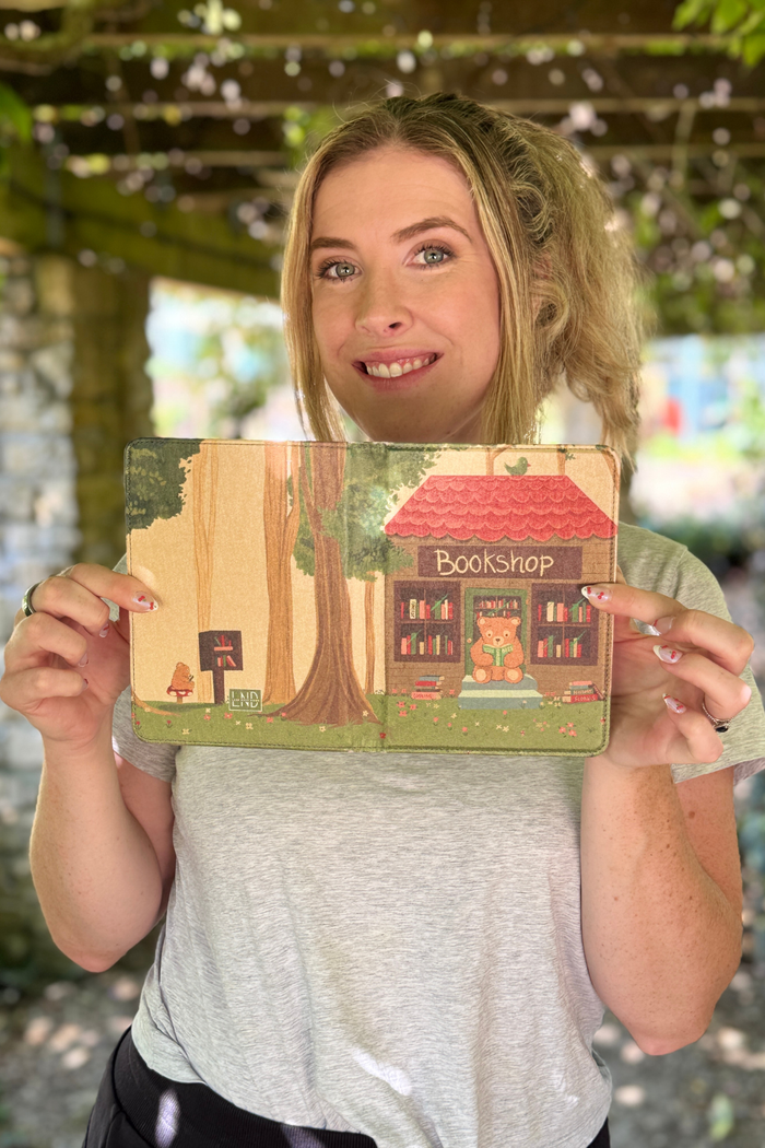 A woman holding a kindle case photographed outdoors under a pergola.