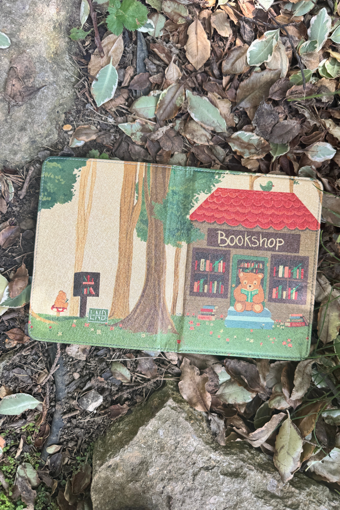 A kindle case lies open on a bed of dry leaves and rocks outdoors.