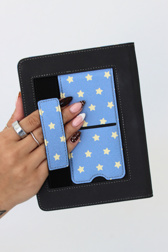Hand holding a kindle case with a star pattern case against a black stand.
