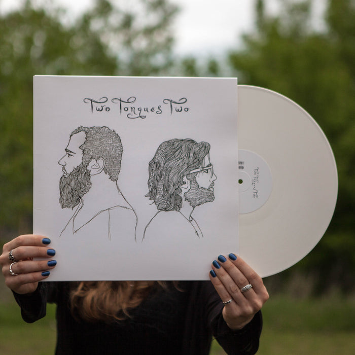 A person holds a White Limited Pressing LP from Two Tongues, its cover featuring line drawings of two bearded men in profile and the band’s name. The person's face is concealed by the bold album artwork.