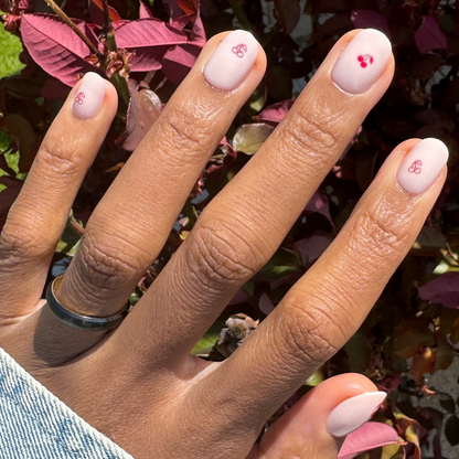Vampy Cherry | Extra Short | Round - Tab Press-On nails in pastel pink with red cherry details on hand outdoors by foliage
