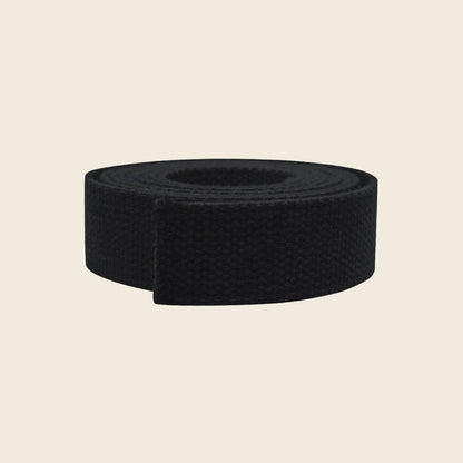 Black woven cotton webbing belly strap for Pilates Cadillac, coiled on a beige background.