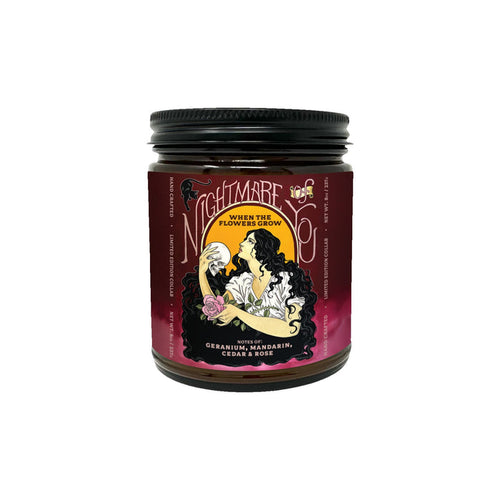 The Nightmare Of You floral candle comes in a dark red jar labeled “Nightmare Before Coffee: When the Flowers Grow,” featuring a woman with flowers. Enjoy scent notes of geranium, mandarin, cedar, and rose for a beautiful fragrance experience.