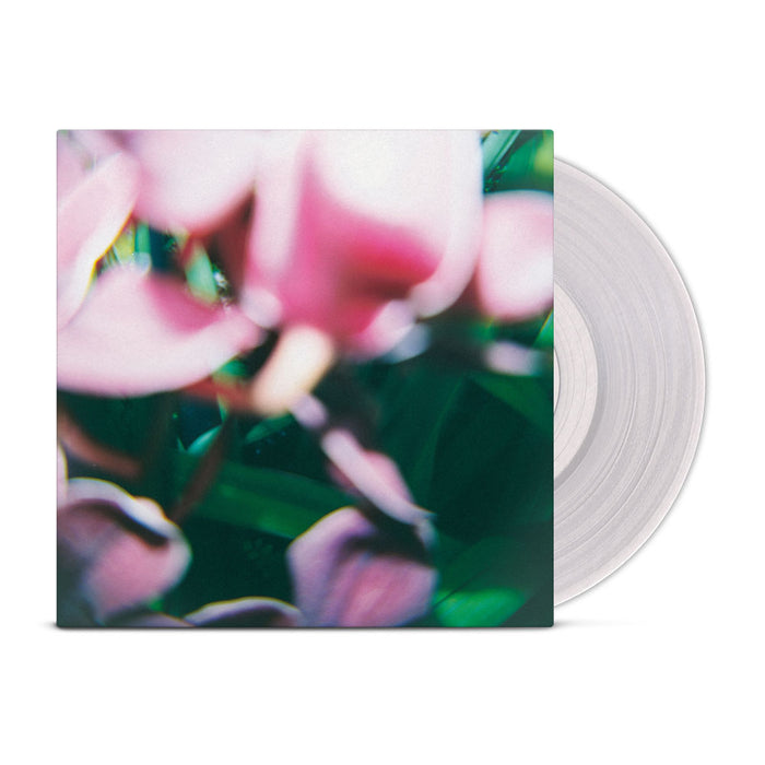 A translucent vinyl record partially slides out of a square Trade Wind LP cover featuring a blurred, abstract design with pink flowers and green foliage.
