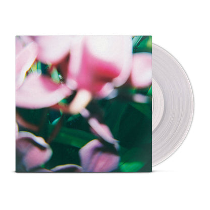 A translucent vinyl record partially slides out of a square Trade Wind LP cover featuring a blurred, abstract design with pink flowers and green foliage.